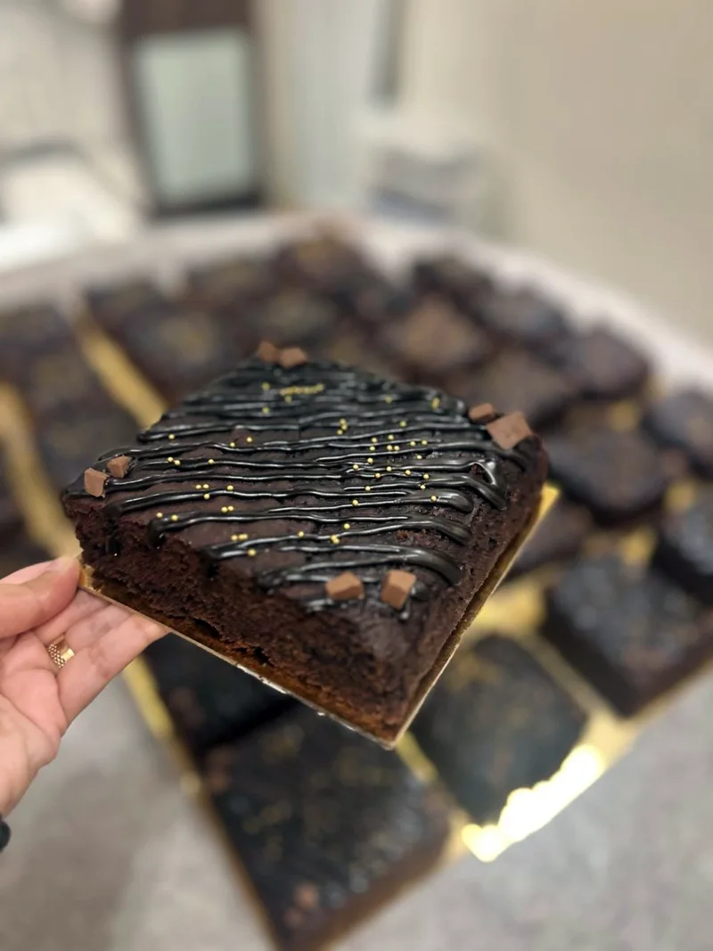 A brownie on a gold board, drizzled with chocolate and topped with chocolate chunks and gold pearls