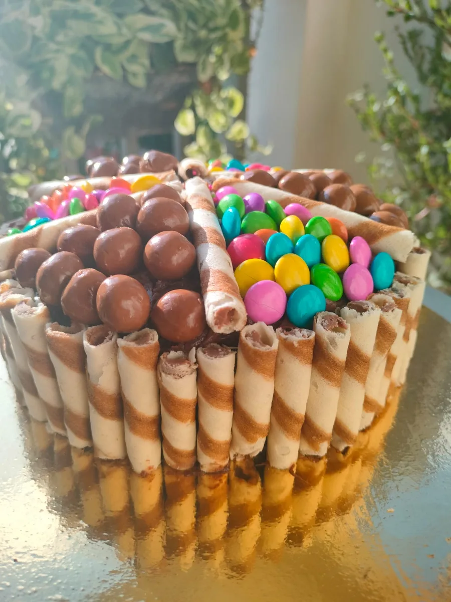 A chocolate cake wrapped in wafer rolls and topped with chocolate balls and coloured gems