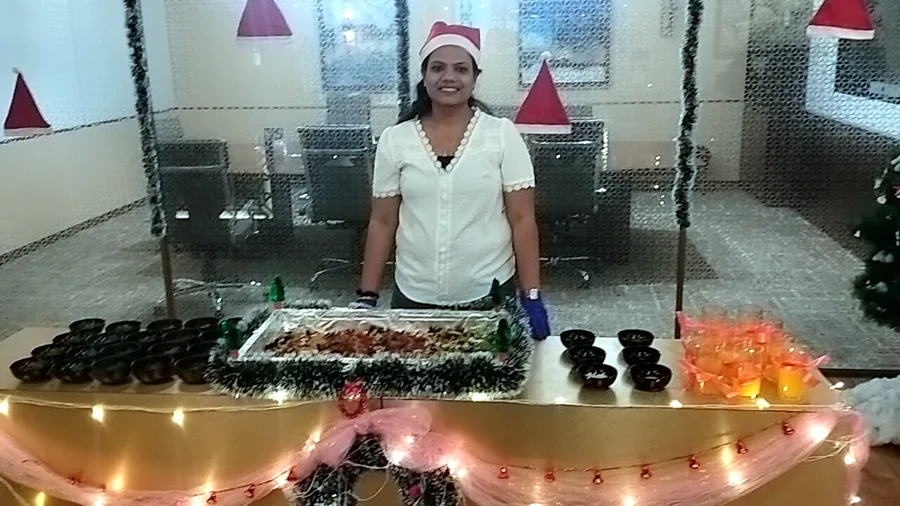 Neha in a Santa hat behind a decorated cake-mixing table at a client office